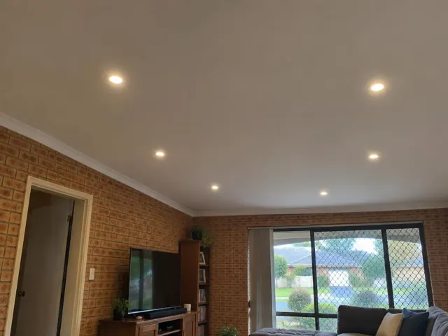 Ceiling with recessed downlights in a brick-walled living room with TV and sliding glass door in Lake Haven