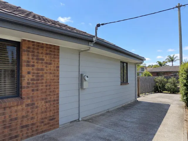 Overhead service cable and point-of-attachment bracket on a suburban brick-and-clad house in Gorokan