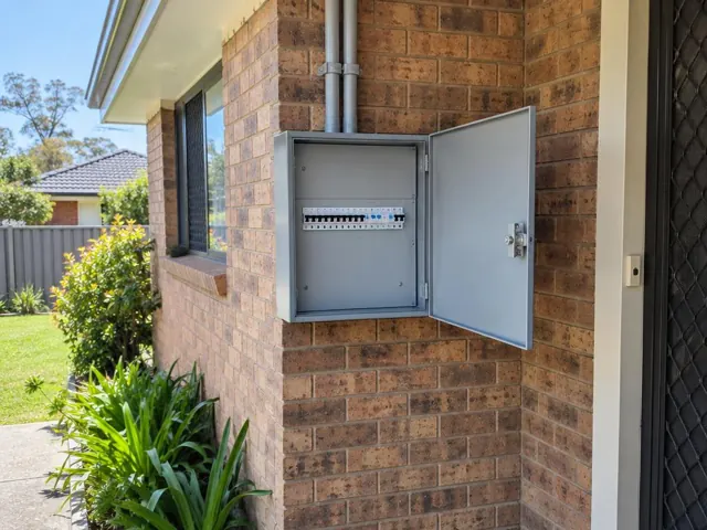 Open external switchboard on a brick house wall beside a doorway in Wadalba